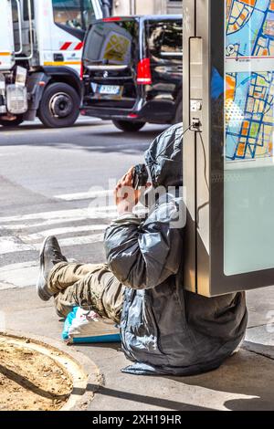 Der Obdachlose saß auf dem Bürgersteig, und das Telefon war an die Bushaltestelle angeschlossen - Paris 75004, Frankreich. Stockfoto