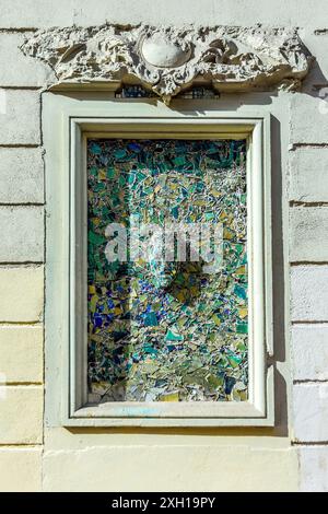 BAS-Reliefbild aus gebrochenen farbigen Fliesen und Glas in alter Fensteröffnung - Paris 75004, Frankreich. Stockfoto