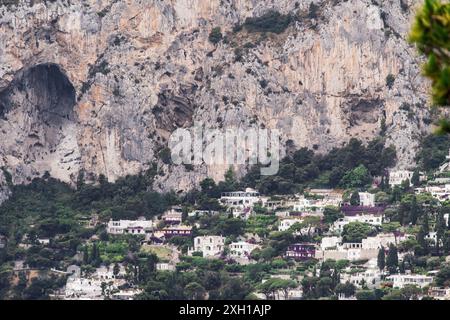 Häuser am Hügel, eingebettet zwischen üppigem Grün am Fuße der zerklüfteten Klippen, bieten eine malerische und dramatische Landschaft auf Capri Island, Italien. Stockfoto