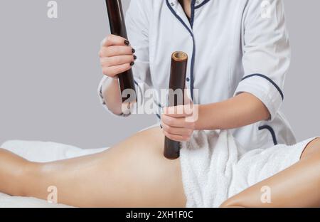 Der Masseur nimmt in einem Schönheitssalon eine Anti-Cellulite-Massage mit Bambusstäben an Oberschenkeln, Beinen und Gesäß vor. Cellulite und Ubergewicht. Stockfoto