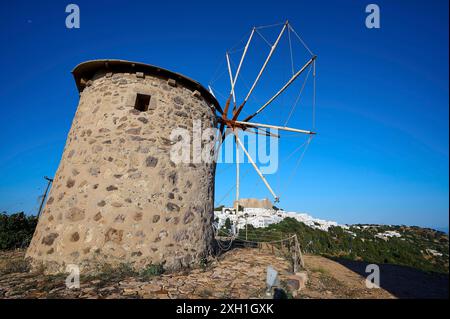 Alte Steinwindmühle unter einem klaren blauen Himmel mit einem Dorf im Hintergrund, Windmühlen, auf einem Kamm, oberhalb von Chora, Hauptstadt Patmos, Patmos, Altstadt Stockfoto