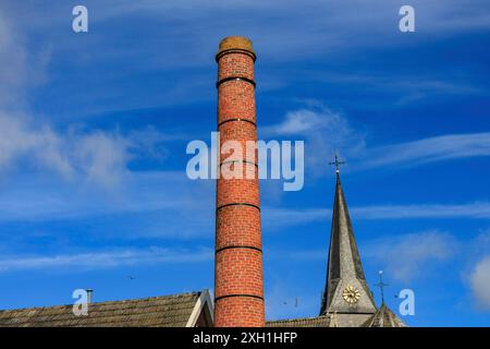 Türmender roter Kamin und Kirchturm mit einer Uhr vor blauem Himmel, Bredevoort, gelderland, niederlande Stockfoto