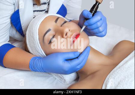 Permanent Make-up für Lippen der schönen Frau im Schönheitssalon. Nahaufnahme-Kosmetikerin, die Lippen tätowiert. Nahaufnahme des Gesichts. Make-up und Kosmetologiekonzept. Stockfoto