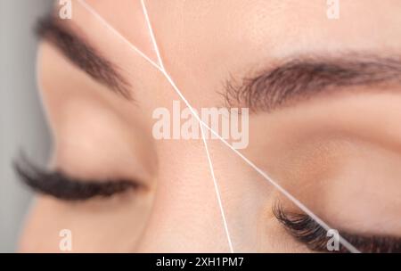 Der Schminkkünstler zupft Augenbrauen mit einer Fadennaht. Frauenkosmetologie im Schönheitssalon. Stockfoto