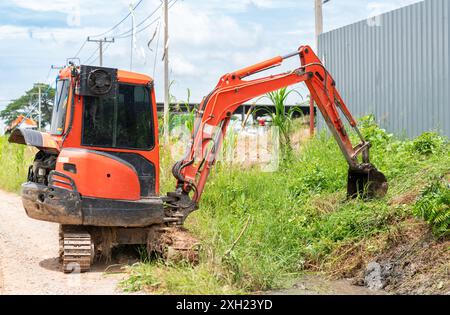 Minibagger graben Entwässerungskanal und klares Gras auf einer Baustelle. Bauarbeiten Stockfoto