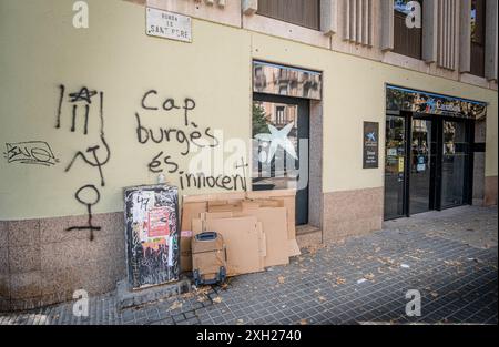 11. Juli 2024, Barcelona, Katalonien, Spanien: Ein Paket und ein Koffer eines Obdachlosen werden an der Tür eines Bankbüros mit Graffiti an der Wand gesehen, die uns daran erinnern, dass es keinen unschuldigen Bourgeois gibt. Die jüngste Zählung der Arrel Foundation schätzt die Anzahl der Menschen, die auf den Straßen Barcelonas schlafen, vor allem im historischen Viertel der Stadt. Gestern hat der Stadtrat von Barcelona ein Investitionshaushalt in Höhe von 228 Millionen Euro vorgelegt, mit dem vorrangig die Bekämpfung von Obdachlosen zum Ziel hat. (Credit Image: © Paco Freire/SOPA images via ZUMA Press Wire) REDAKTIONELLE VERWENDUNG ONL Stockfoto