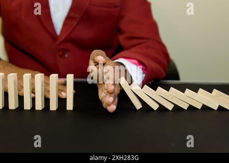 Eine Nahaufnahme der Hand eines Geschäftsmannes, die einen Domino-Effekt verhindert. Ein überzeugendes Bild von Risikomanagement und Problemlösung. Stockfoto