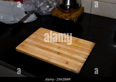 Abgenutztes Holzschneidebrett auf einer sauberen schwarzen Arbeitsplatte, bereit für kulinarische Kreationen. Stockfoto