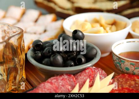 Oliven, Wurst und Käse auf einem Serviergericht mit Honig auf einem rustikalen Tisch. Mediterrane Vorspeise mit Oliven auf einem Serviergericht Stockfoto