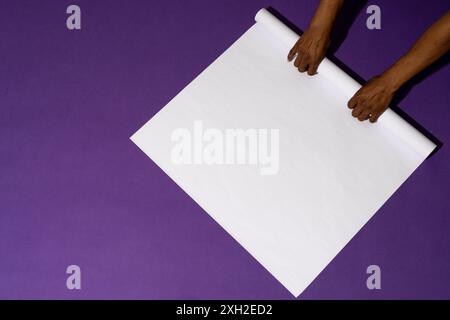 Hände Rollen ein leeres weißes Poster auf violettem Hintergrund mit Platz für das Kopieren aus. Das Bild erfasst einen Moment der Vorbereitung für eine Präsentation oder ein Bildmaterial Stockfoto