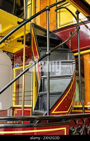 Vintage Wendeltreppe in einer farbenfrohen alten Straßenbahn mit satten Gelb- und Rottönen, die den historischen Charme der öffentlichen Verkehrsmittel widerspiegelt. Stockfoto