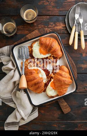 Croissants, englisches Frühstück. Köstliches frisches Frühstück gegrillt drei Croissants mit Speck, Spiegeleiern und Bohnen in Tomatensauce und zwei Gläsern C. Stockfoto