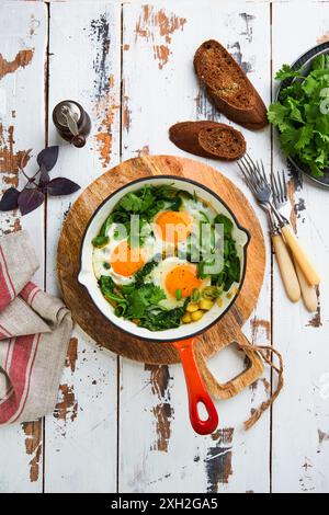 Grüne Shakshuka. Spiegeleier, Kartoffeln, Spinat und Zwiebeln in roter gusseiserner Pfanne mit Roggenbrot auf einem alten Vintage-Tisch Hintergrund. Traditionell Jüdisch, Stockfoto