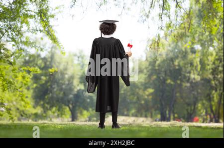 Rückansicht eines männlichen Schülers in einem Abschlusskleid, der in einem Park steht Stockfoto