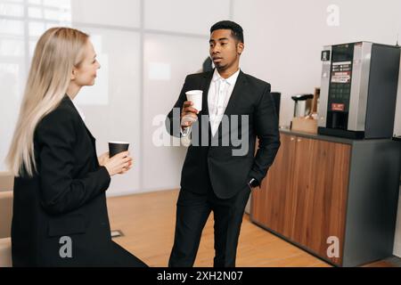 Verschiedene Geschäftsleute im Anzug, die eine Kaffeepause machen und sich im Büro unterhalten. Glückliche männliche weibliche Angestellte genießen Kaffeepause drinnen. Stockfoto