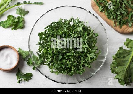 Gehackter frischer Grünkohl in einer transparenten Salatschüssel für die Zubereitung eines gesunden Salats auf einem hellgrauen Hintergrund, Ansicht von oben, Nahaufnahme Stockfoto