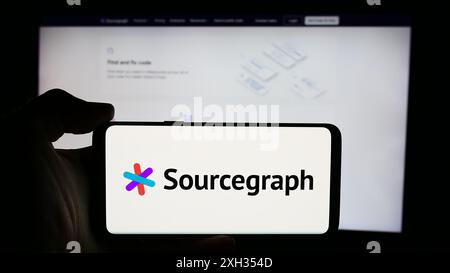 Person, die ein Mobiltelefon mit dem Logo des US-amerikanischen Code Intelligence-Unternehmens Sourcegraph Inc. Vor der Business-Website hält. Schwerpunkt auf dem Display des Telefons. Stockfoto