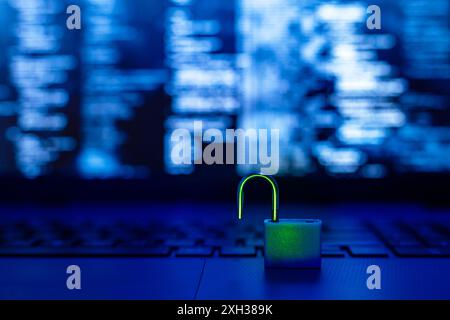 Ein entsperrtes Vorhängeschloss befindet sich auf einer dunklen Laptop-Tastatur, auf dem ein blauer Bildschirm Code im Hintergrund anzeigt. Stockfoto