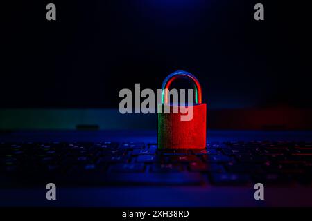 Ein geschlossenes Vorhängeschloss befindet sich auf einer dunklen Laptop-Tastatur, die von rotem und blauem Licht beleuchtet wird. Stockfoto