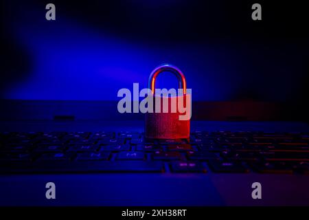 Ein geschlossenes Vorhängeschloss befindet sich auf einer schwarzen Laptop-Tastatur, die von blauem und rotem Licht beleuchtet wird. Stockfoto