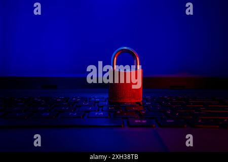 Ein rotes Vorhängeschloss befindet sich auf einer Laptop-Tastatur, die von blauem und rotem Licht beleuchtet wird. Stockfoto