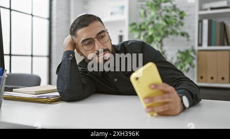 Hübscher arabischer Mann in Brille mit Smartphone am Schreibtisch Stockfoto