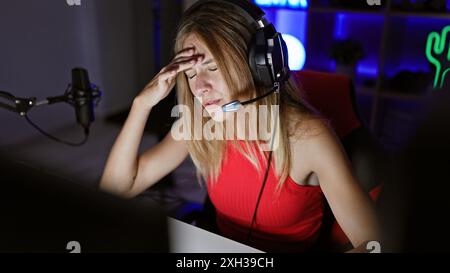 Eine gestresste junge Frau, die nachts in einem dunklen Spielzimmer Kopfhörer trägt. Stockfoto