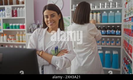 Zwei lachende spanische Apothekerinnen in weißen Mänteln arbeiten in einem gut organisierten Drogeriemarkt zusammen, eine blickt auf die Kamera und die andere auf Stockfoto