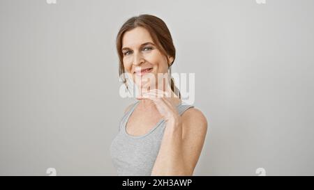 Eine selbstbewusste Frau mittleren Alters mit kurzen Haaren posiert in einem ärmellosen Oberteil vor weißem Hintergrund. Stockfoto