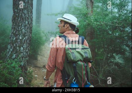 Ein Mann mit Hut und Rucksack geht durch einen nebeligen Wald. Die nebelige Atmosphäre trägt zum Gefühl des Abenteuers und der Einsamkeit in der Natur bei. Stockfoto