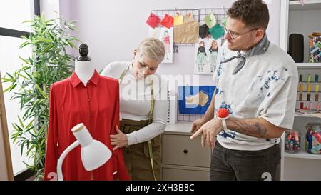 Zwei Schneider, eine Frau und ein Mann, arbeiten in einem hellen Atelier zusammen und untersuchen ein Kleid an einer Schaufensterpuppe. Stockfoto