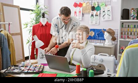 Zwei Schneider, ein Mann und eine Frau, arbeiten in einem farbenfrohen Schneiderstudio mit Modeschmustern zusammen. Stockfoto