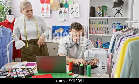 Zwei Modedesigner, eine Frau und ein Mann, arbeiten zusammen in einer Schneiderei mit Stoff und Nähmaschine. Stockfoto