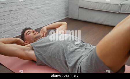 Gutaussehender Mann, der auf einer rosafarbenen Matte in einem stilvollen Wohnzimmer trainiert, verkörpert moderne Fitness und gesunden Lebensstil zu Hause. Stockfoto