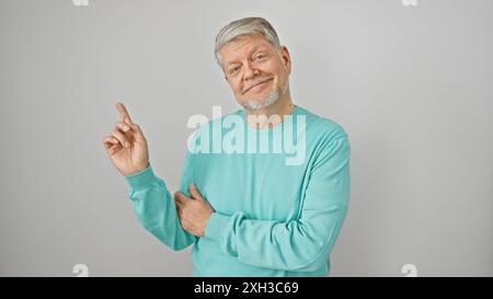Lächelnder älterer Mann in türkisfarbenem Pullover isoliert auf weißem Hintergrund, der mit Zeigefinger zeigt Stockfoto