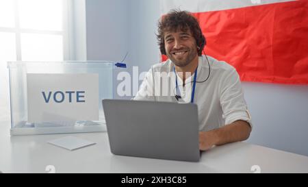 Hübscher junger Mann, der an einem Laptop in einem Wahlstudienzimmer mit polnischer Flagge arbeitet Stockfoto