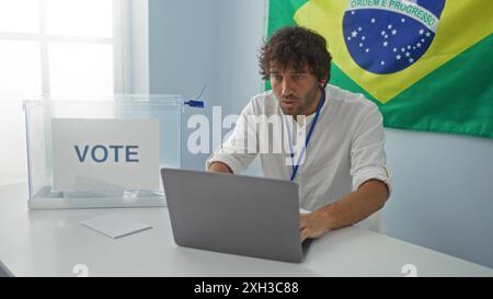 Junger Mann, der an einem Schreibtisch sitzt, mit einem Laptop, einer Wahlbox und einer brasilianischen Flagge im Hintergrund, die eine Wahlsituation in brasilien repräsentiert Stockfoto