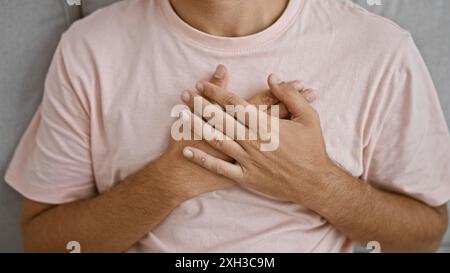 Nahaufnahme eines jungen latino-Mannes in einem rosa Hemd drinnen, der seine Hände vor seiner Brust umklammert und Emotionen zeigt. Stockfoto