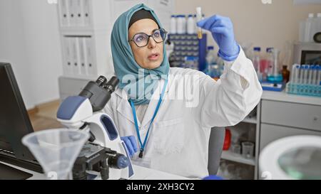 Eine Frau mittleren Alters im Hijab untersucht ein Reagenzglas in einem modernen Labor und zeigt die Vielfalt der Wissenschaft. Stockfoto