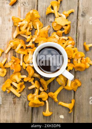 Eine weiße Tasse Kaffee und Tee umgeben von vielen Waldpilzen auf dem Hintergrund von altem Holz Stockfoto