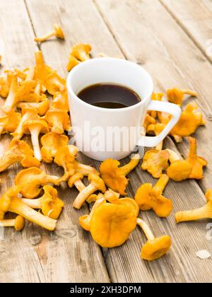 Eine weiße Tasse Kaffee und Tee umgeben von vielen Waldpilzen auf dem Hintergrund von altem Holz Stockfoto