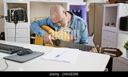 Glatzkopf spielt Akustikgitarre in einem modernen Büro mit Mikrofon und Computerpult. Stockfoto