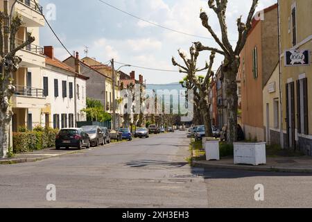 Langeac, Frankreich - 28. Mai 2023: Eine ruhige Straße in Langeac, Frankreich, mit Reihen parkender Autos und traditionellen Häusern. Üppige Bäume säumen die Straße, Providin Stockfoto