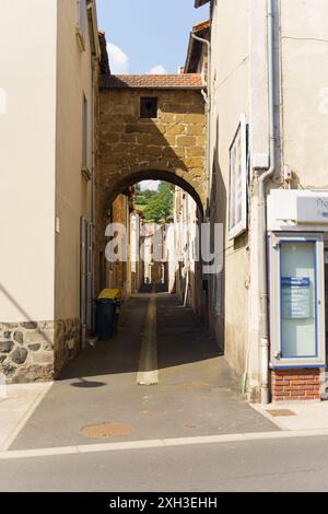 Langeac, Frankreich - 28. Mai 2023: Eine enge Kopfsteinpflasterallee in Langeac, Frankreich, gesäumt von alten Steinhäusern und einem bogenförmigen Durchgang. Der Sonnenschein Stockfoto