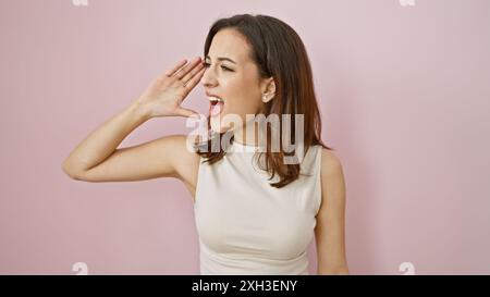 Eine fröhliche hispanische Frau mit einem lebhaften Ausdruck, der gegen eine rosa Wand schreit Stockfoto