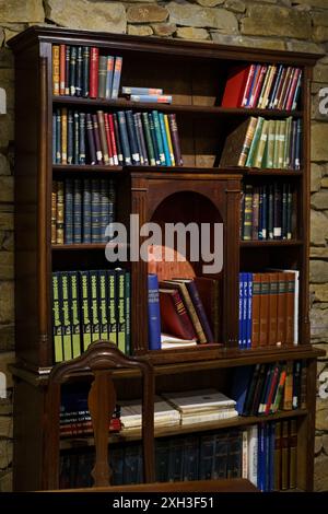 Astorga, Spanien - 4. Juni 2023: Ein Vintage-Holzregal, das mit Büchern überflutet ist, steht an einer Steinmauer in Astorga, Spanien. Stockfoto