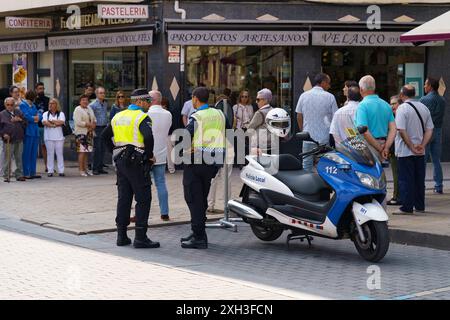 Astorga, Spanien - 4. Juni 2023: Zwei Polizeibeamte in Uniform stehen auf einer Stadtstraße in Astorga, Spanien, neben ihrem Roller. Eine Gruppe von Leuten beobachtet Stockfoto
