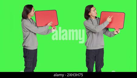 Junger Erwachsener posiert mit Sprechblase und zeigt leere Plakate mit Copyspace vor dem Hintergrund des Grünbildes. Asiatisches männliches Modell, das Pappe für Werbeanzeigen im Studio hält. Stockfoto