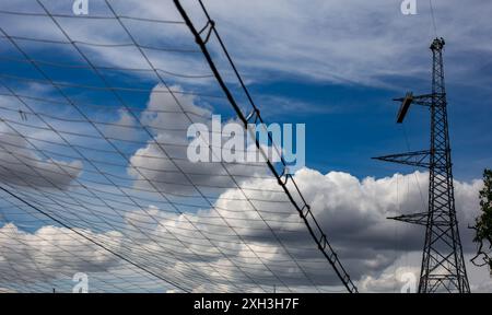 Arbeiter in gut sichtbarer Kleidung auf einem elektrischen Pylonturm vor bewölktem Himmel mit Kabelschutznetz Stockfoto