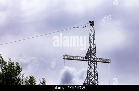 Arbeiter, die unter bewölktem Himmel Wartungsarbeiten an der Spitze einer hohen Seilbahn durchführen Stockfoto